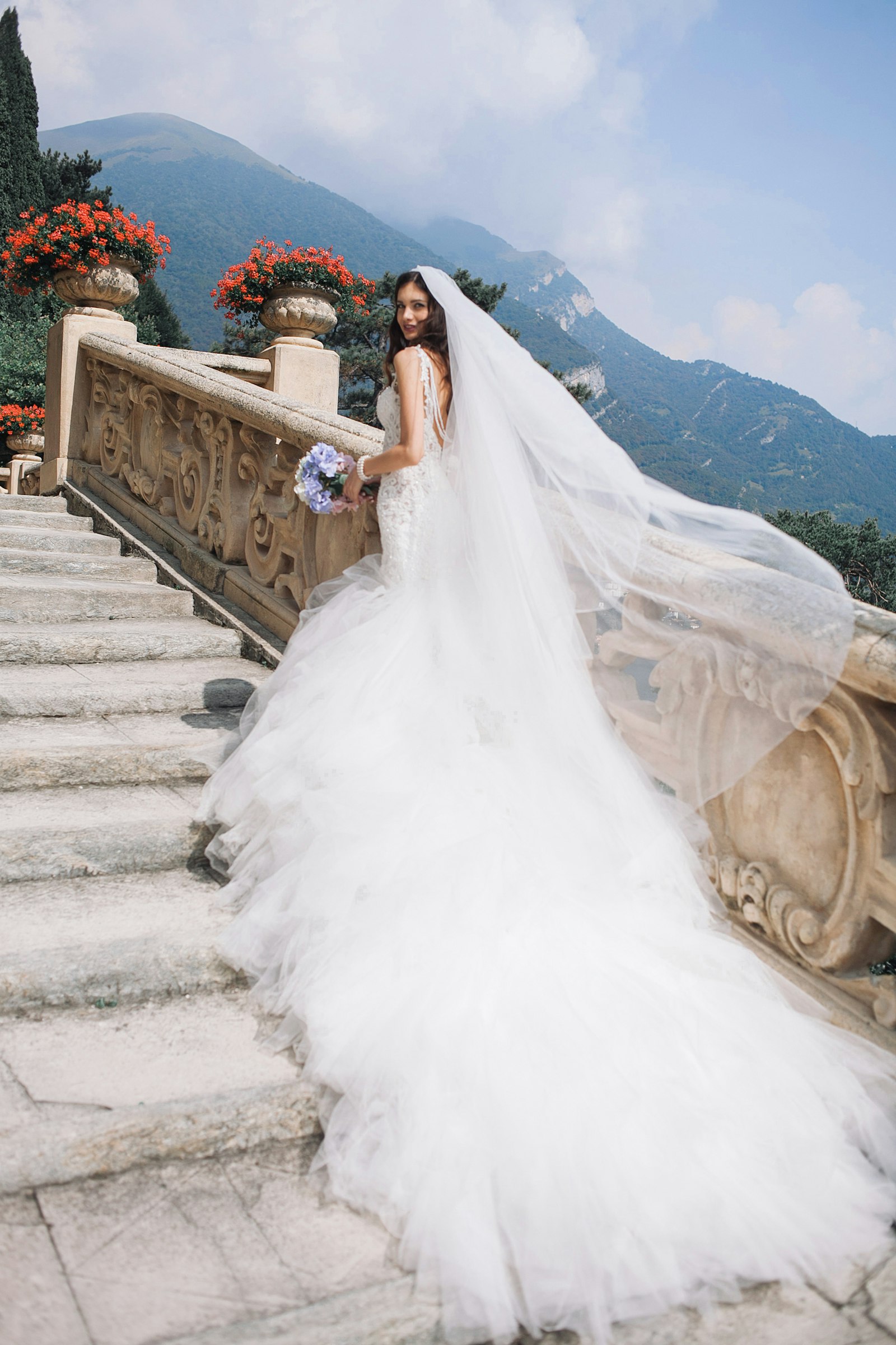 Braut im weißen Kleid mit Brautstrauß auf einer hellen Treppe