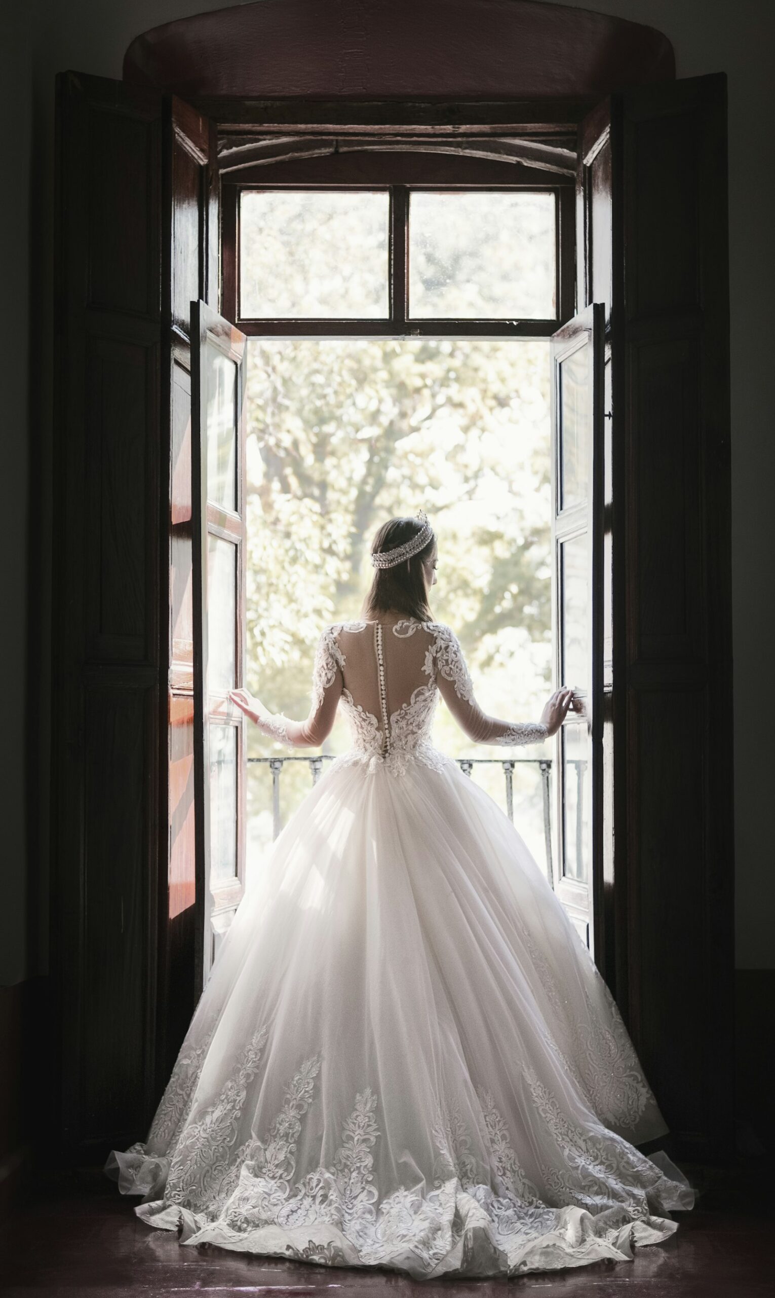Braut im weißen Kleid steht am Fenster